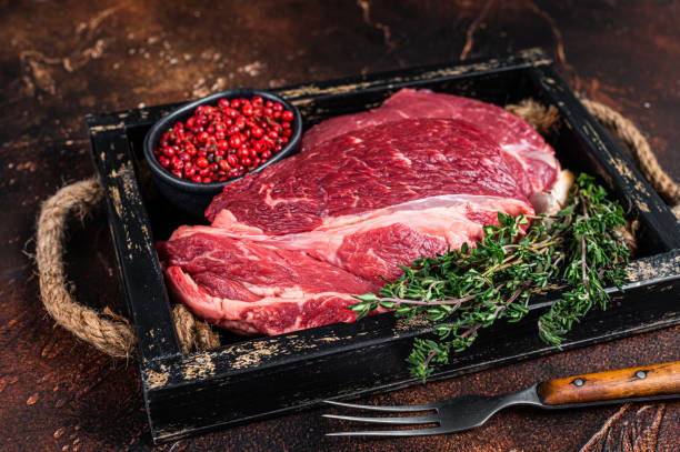 Fresh Raw Chuck eye roll beef steak in a wooden tray with herbs. Dark background. Top view Fresh Raw Chuck eye roll beef steak in a wooden tray with herbs. Dark background. Top view. boneless chuck steak stock pictures, royalty-free photos & images