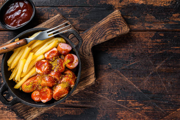 comida callejera currywurst, especias de curry en wursts servidas papas fritas en una sartén. fondo de madera oscura. vista superior. espacio de copia - currywurst fotografías e imágenes de stock