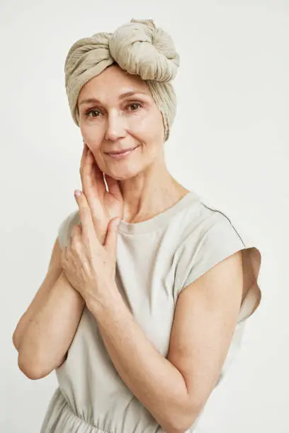Minimal portrait of beautiful mature woman wearing headscarf and posing against white background