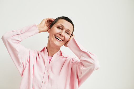 Minimal portrait of carefree mature woman with short haircut looking at camera while wearing pink dress shirt