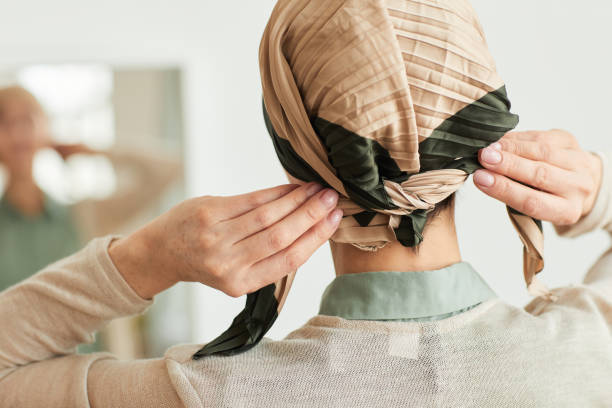 Woman Wearing Headscarf Back view at mature woman putting on headscarf by mirror and getting ready to go out, copy space survival stock pictures, royalty-free photos & images