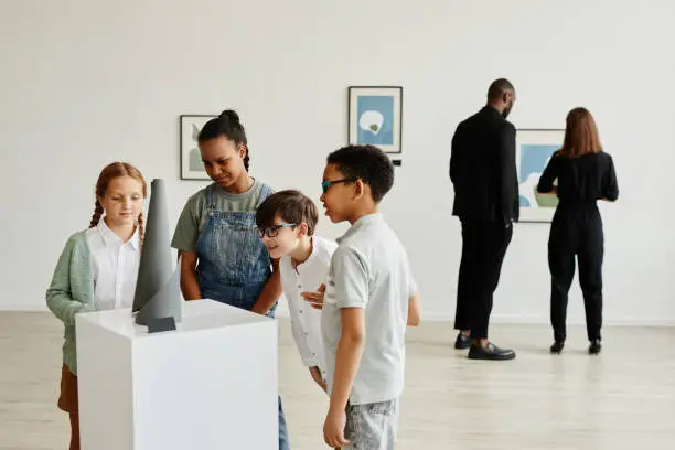 Multi-ethnic group of children looking at sculptures in modern art gallery, copy space