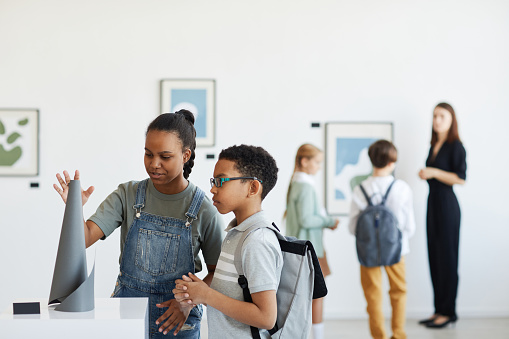 Minimal portrait of schoolchildren visiting art gallery and looking at modern sculptures, copy space