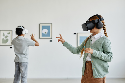 Minimal side view at cute girl wearing VR headset in art gallery while enjoying immersive experience, copy space