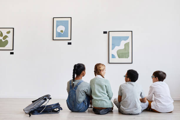 Kids Looking at Abstract Paintings Back view at diverse group of children sitting on floor in modern art gallery and discussing paintings, copy space child art people contemporary stock pictures, royalty-free photos & images