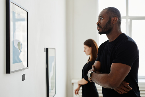 Minimal side view portrait of African-American man looking at paintings in modern art gallery, copy space