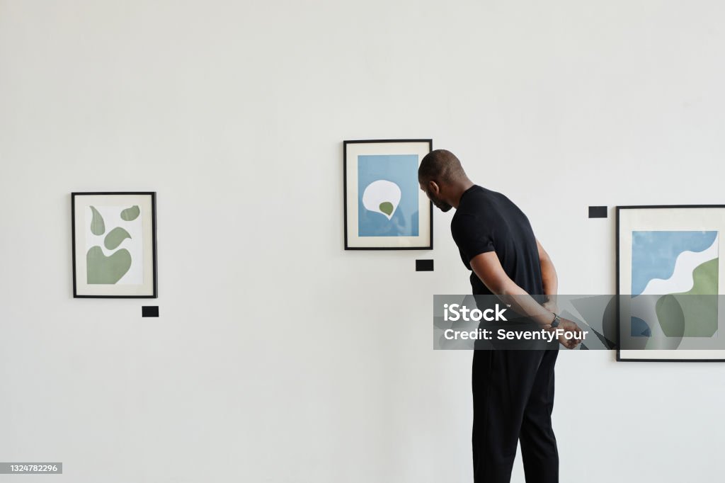 African American Man in Art Gallery Minimal back view at African-American man looking at paintings in modern art gallery, copy space Art Museum Stock Photo