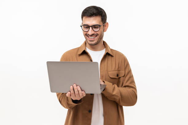 istock Young happy man standing with opened laptop, browsing online or typing message, isolated on gray background 1324786395