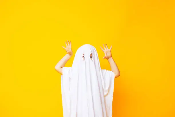 Little kid wearing cute halloween ghost costume on yellow background.