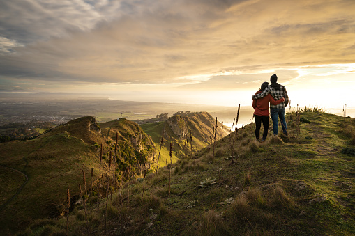 Man and woman embracing each other on the peak on a mountain while contemplating the landscape. Horizontal photography
