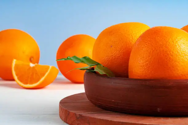 Whole ripe oranges in a clay bowl on white table close up
