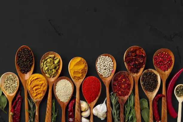 Various exotic spices in wooden spoons on dark background, view from above