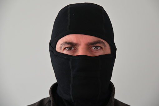 Portrait of a serious man (male age 40-50) wearing black face mask looking at camera.