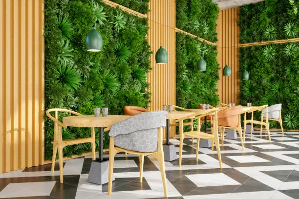 Photo of Modern Cafe Interior With Wooden Table, Chairs And Vertical Garden. Eco-Friendly Cafe With Creeper Plant On The Wall