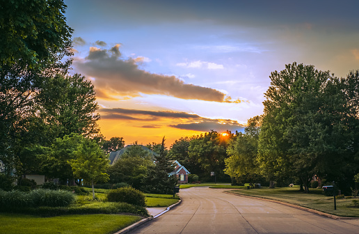 View of street in suburban Midwestern neighborhood in summer; sunset sky in background