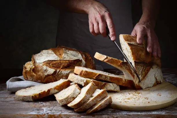 Photo of Male hands cutting loaf of bread on wooden chopping board, close-up, space for text.