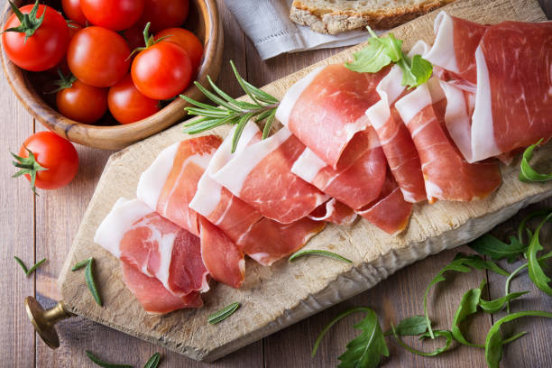 сырая ветчина с помидорами церри на деревянной разделоной доске, вид сверху. - prosciutto ham meat parma ham стоковые фото и изображения