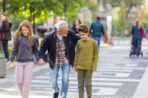 An Older Man is Enjoying the Time with his Grandchildren While Holding Hands and Walking Through the City Streets.