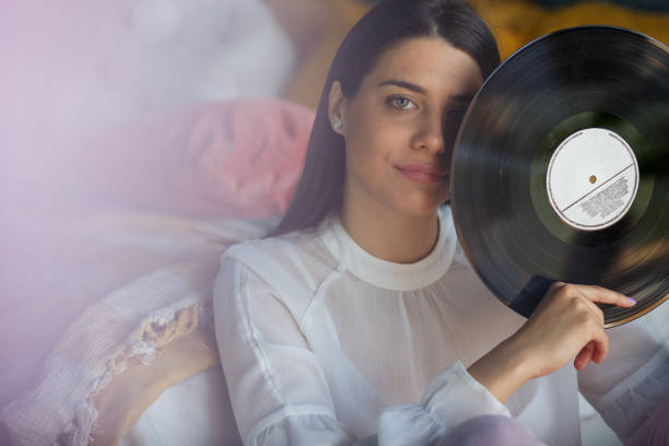 vista frontal de una mujer joven sosteniendo un disco de vinilo y mirando a la cámara - disco audio analógico fotografías e imágenes de stock