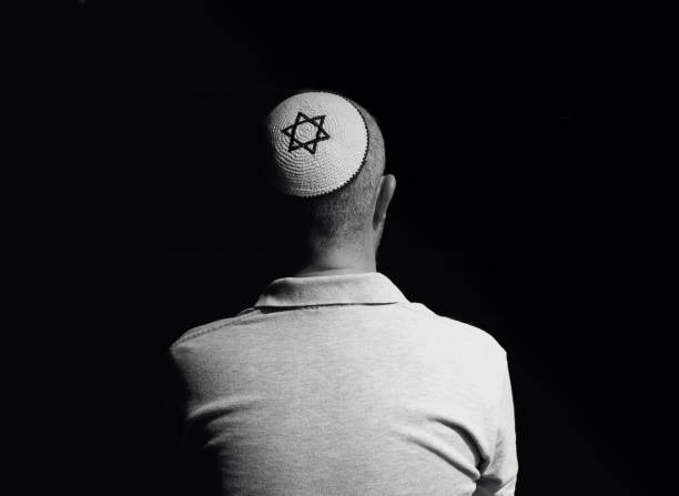 istock Young Jewish man wearing skull cap praying inside synagogue 1324830944