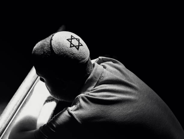 Young Jewish man wearing skull cap praying inside synagogue
