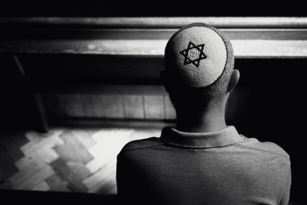 istock Young Jewish man wearing skull cap praying inside synagogue 1324830955