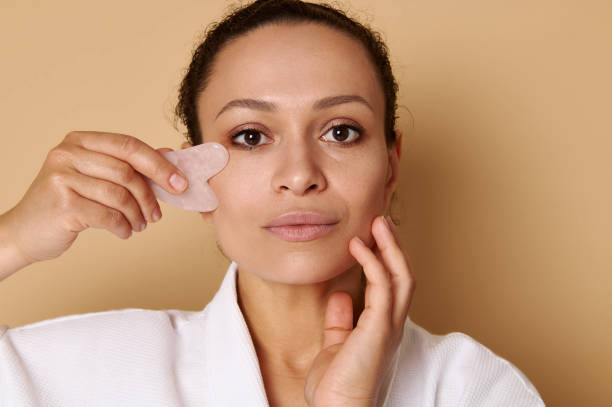 retrato de beleza de mulher mestiça usando gua-sha para massagem facial de drenagem linfática. spa e conceitos de cuidados com a pele. headshot - spooning - fotografias e filmes do acervo