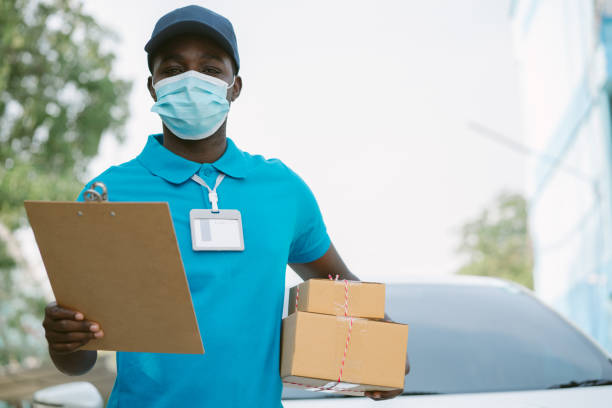 African delivery man holding boxs and cardboard with wearing face mask stock photo