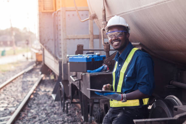 African machine engineer technician wearing a helmet, groves and safety vest is using a wrench to repair the train with using tablet stock photo