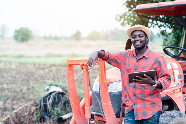 African man farmer working in the field with a tractor and using tablet stock photo