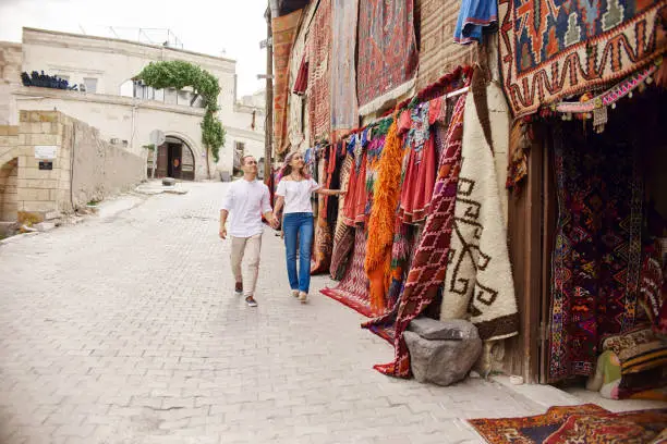 Photo of Couple in love buys a carpet and handmade textiles at an oriental market in Turkey. Hugs and cheerful happy faces of men and women