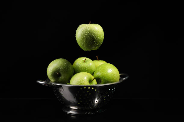 istock Green apple with water drops falling down into colander on black background 1324840085