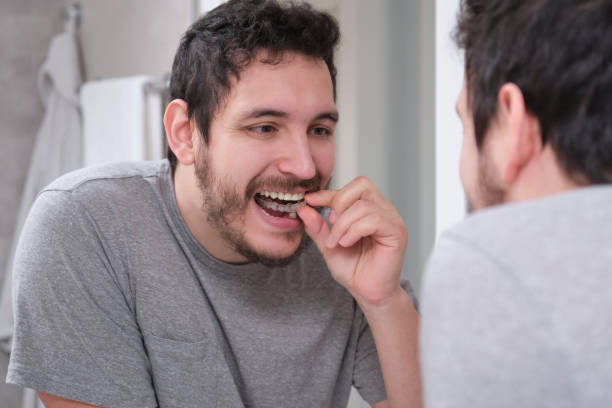 istock Young latin man putting orthodontic silicone trainer or invisible braces aligner in front of the mirror. Mobile orthodontic appliance for dental correction. 1324842896