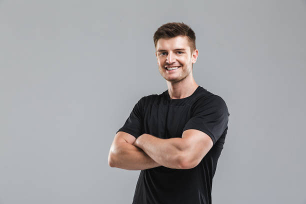 Portrait of a smiling young sportsman Portrait of a smiling young sportsman standing with arms folded isolated over gray background isolated color stock pictures, royalty-free photos & images