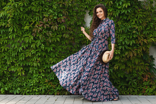 Portrait of gorgeous woman wearing beautiful maxi dress posing against wall with a wild grape