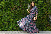 Gorgeous woman wearing beautiful maxi dress posing against wall with a wild grape
