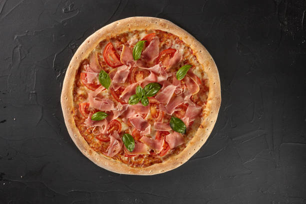 istock Pizza with tomatoes, prosciutto, basil on black background 1324844619