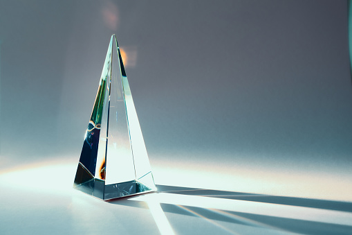 Glass pyramid prism with colorful sunlight reflection on background with copy space, horizontal