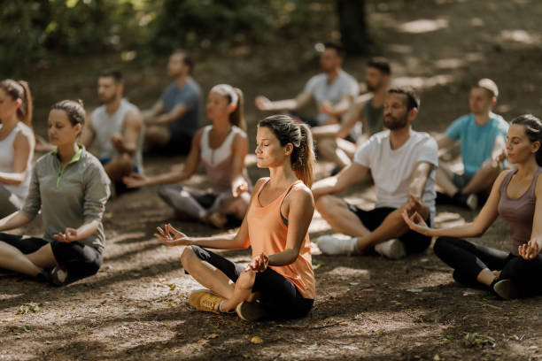 un grande gruppo di atleti che meditano sulla lezione di yoga in natura. - yoga exercising outdoors group of people foto e immagini stock