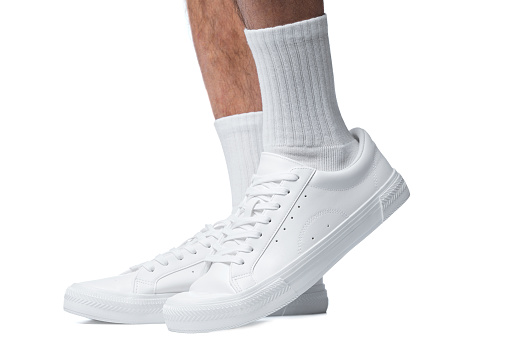 Closeup of male feet and shoes. Man wearing white trainers isolated on white background.