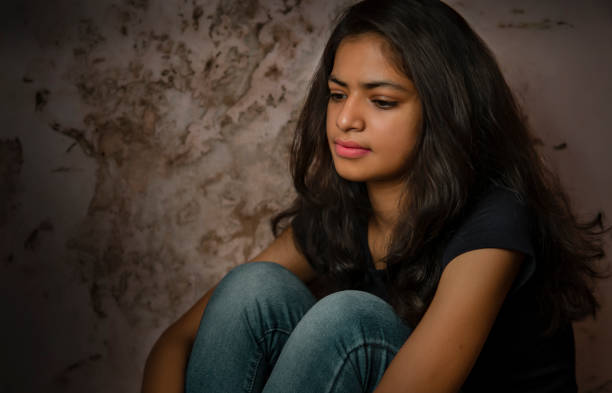 triste, sereno jovem mulher sentado perto da parede suja e contemplando com uma expressão em branco. - teenager dark pensive emotional stress - fotografias e filmes do acervo