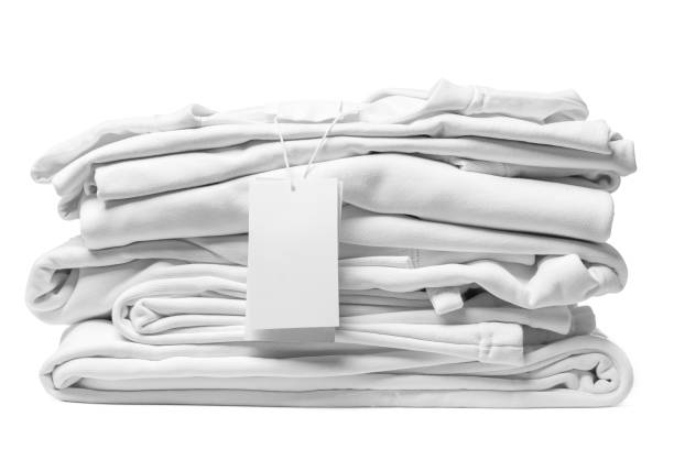 stack of white clothes with a blank garment tag on white background - white clothing imagens e fotografias de stock