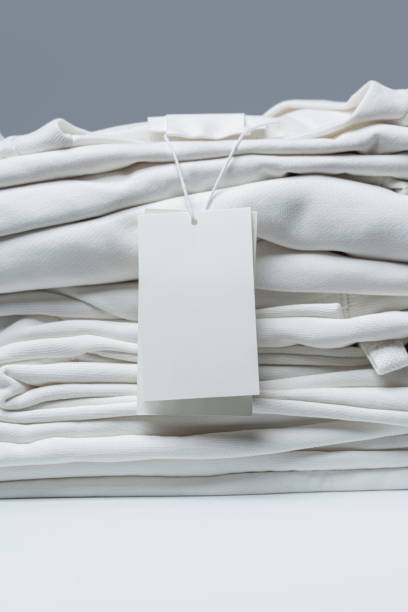 istock Stack of new white clothes with a blank garment tag 1324848283