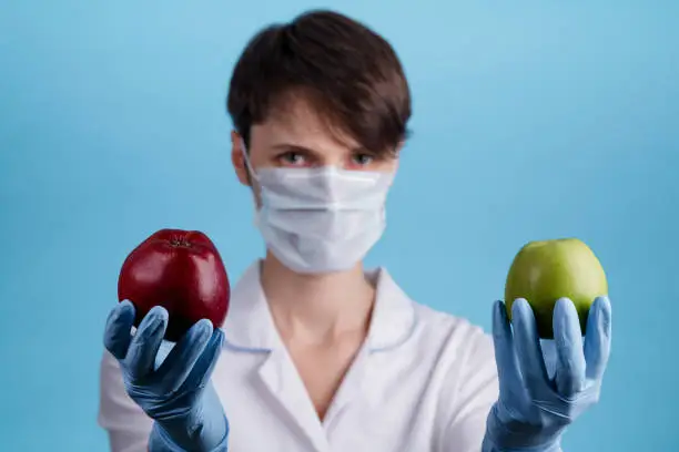 Photo of woman doctor in a medical mask offers a choice of red or green Apple. healthy diet and vitamin replenishment