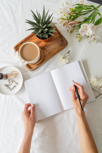 istock Opened book, coffee and flowers top view on white bed. Mock up design 1324850767