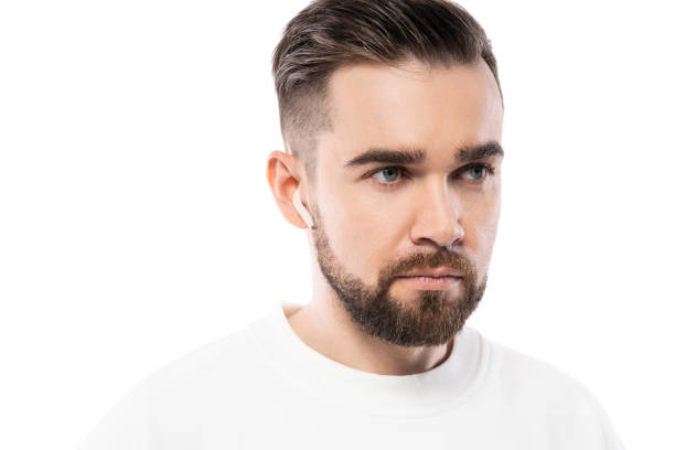 istock Handsome bearded man in white clothes  using wireless earbuds on white background 1324853384