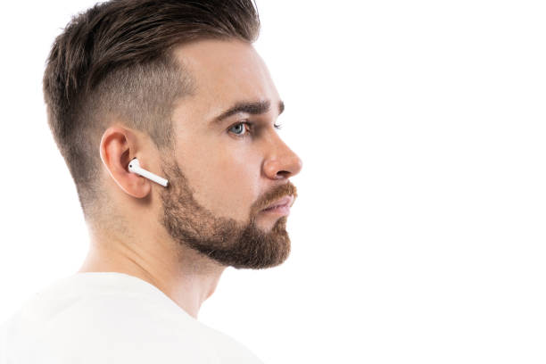 istock Handsome bearded man in white clothes  using wireless earbuds on white background 1324853393