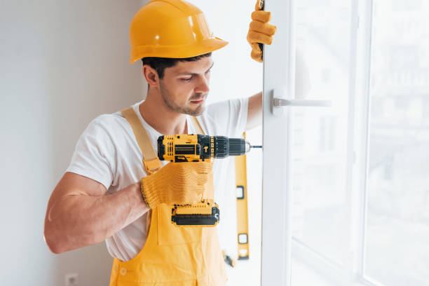 istock Handyman in yellow uniform installs new window by using automatic screwdriver. House renovation conception 1324857586