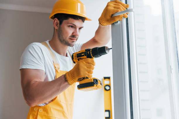 istock Handyman in yellow uniform installs new window by using automatic screwdriver. House renovation conception 1324857694
