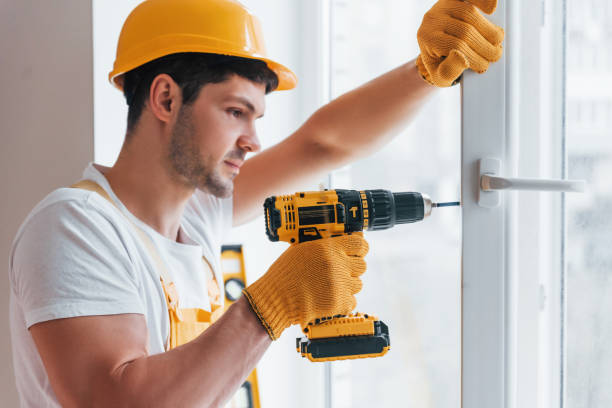 istock Handyman in yellow uniform installs new window by using automatic screwdriver. House renovation conception 1324857697
